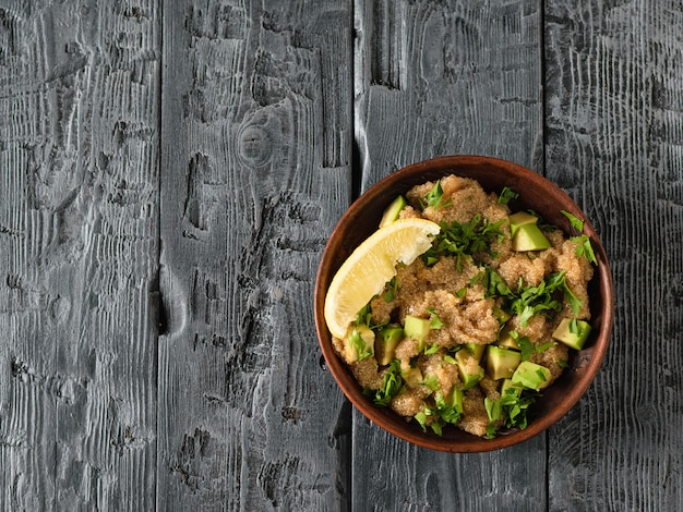 Salad with amaranth, lemon, avocado and parsley in a clay bowl in the right corner of the table