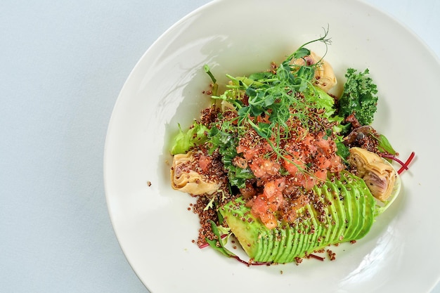 Salad with artichokes, tomatoes, quinoa and avocado in a white plate. Superfood