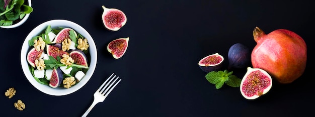 Salad with arugula feta cheese figs and walnuts in the white bowl on the black background Top view Closeup