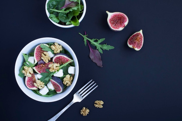 Salad with arugula feta cheese figs and walnuts in the white bowl on the black background Top view Copy space