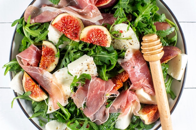 Salad with arugula figs prosciutto and mozzarella on white wooden background