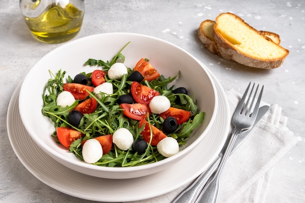 Foto insalata con rucola, mozzarella, pomodori e olive, olio d'oliva e pane fresco