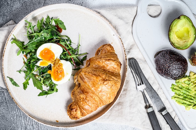 Salad with avocado, arugula, croissant and egg.