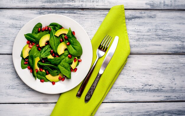 salad with avocado, arugula, spinach, pomegranate, seeds on wooden background