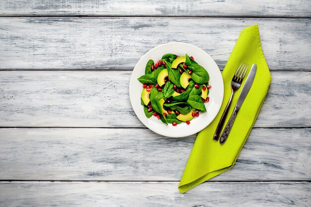 salad with avocado, arugula, spinach, pomegranate, seeds on wooden background