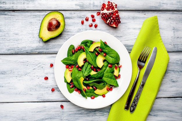 salad with avocado, arugula, spinach, pomegranate, seeds on wooden background