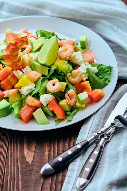 Salad with avocado, feta cheese and shrimps on old wooden table