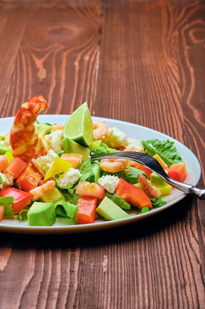 Salad with avocado, feta cheese and shrimps on old wooden table