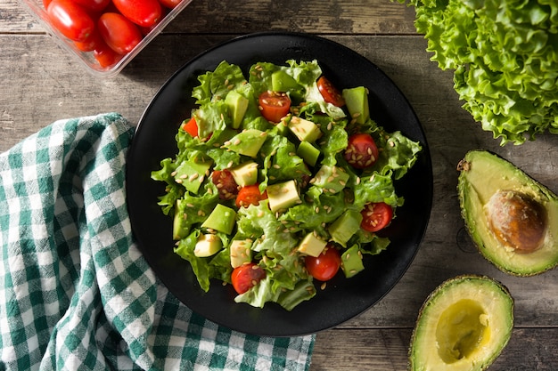 Salad with avocado, lettuce, tomato and flax seeds on wooden table Top view