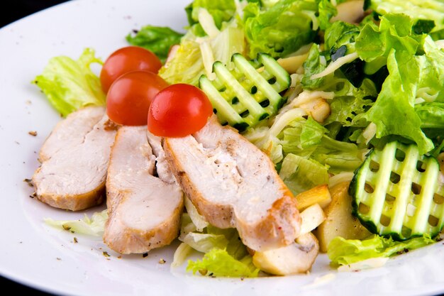 Salad with baked chicken breast: chicken fillet, mushrooms champignon, cucumbers, mozzarella cheese, lettuce leaves, cherry tomatoes. Close up macro