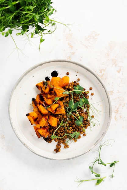 Salad with baked pumpkin, lentils and balsamic dressing garnished with peas microgreens