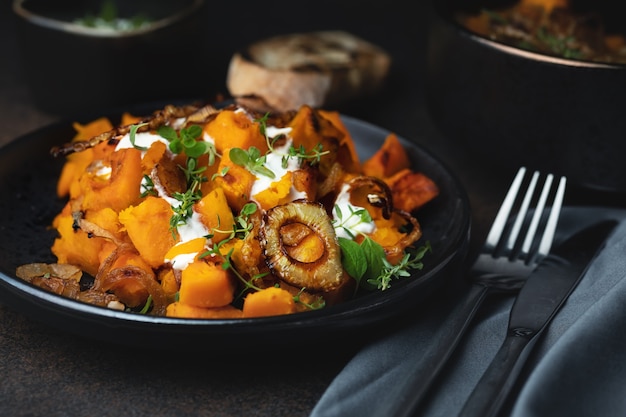 Salad with baked pumpkin, thyme, roasted onion and yogurt sause, a delicious autumn dish. On dark background. Selective focus