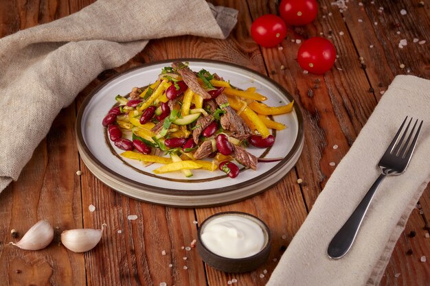 Salad with beans, meat, peppers and cucumber, wooden background