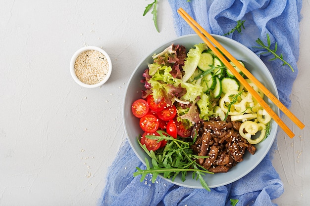 Salad with beef teriyaki and fresh vegetables - tomatoes, cucumbers, paprika, arugula and lettuce in bowl. Flat lay. Top view