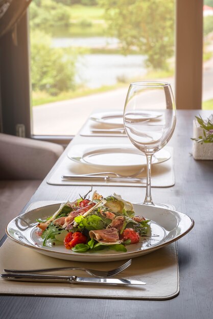 Photo salad with burrata, parma and cherry tomatoes confit in front of a large window