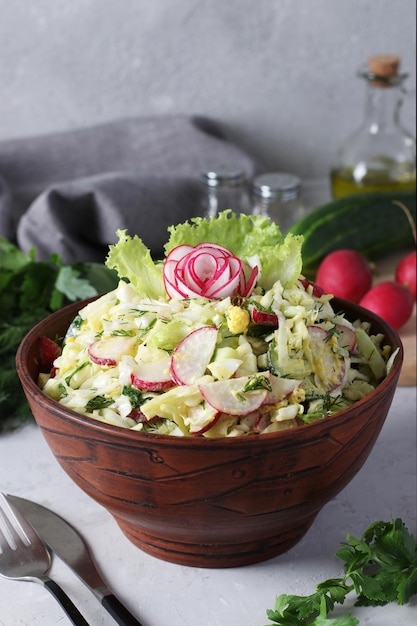 Salad with cabbage cucumbers radishes parsley and egg seasoned with olive oil in a brown bowl