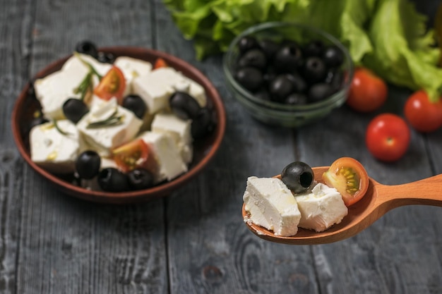 Salad with cheese in a wooden spoon on a wooden table background. Salad with cheese and vegetables.