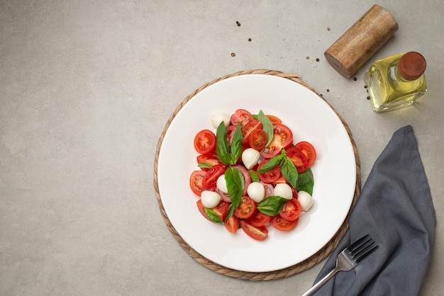 Salad with cherry tomatoes and mozzarella in a white plate on a gray background