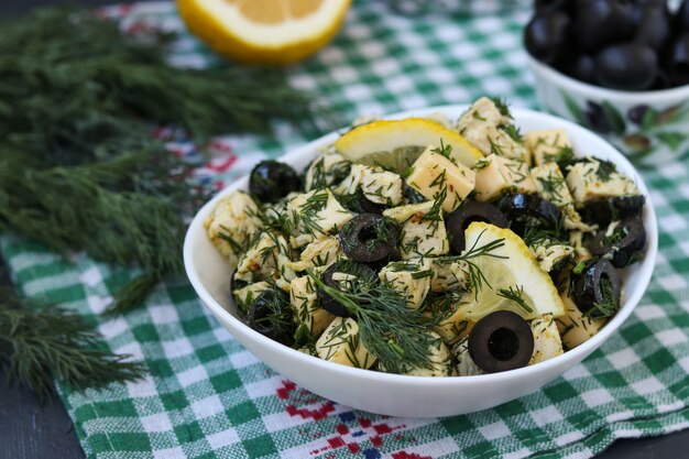 Салат с курицей, сыром и маслинами в белых мисках на столе