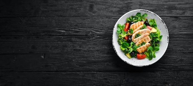 Салат с куриным филе, оливками, помидорами и авокадо в тарелке на деревянном фоне Вид сверху Свободное место для текста Плоская планировка