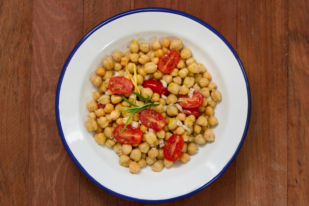 Salad with chickpea and tomato on white dish on brown wooden surface