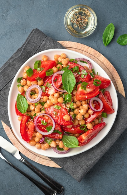 Salad with chickpeas, tomatoes and basil in a white plate on a dark background. Healthy food. Vertical view.