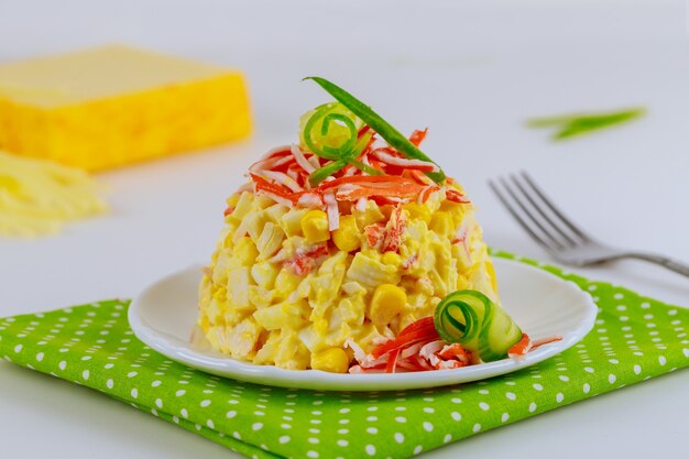 Insalata con bastoncini di granchio, cetriolo, uova e mais sul piatto bianco con forchetta.