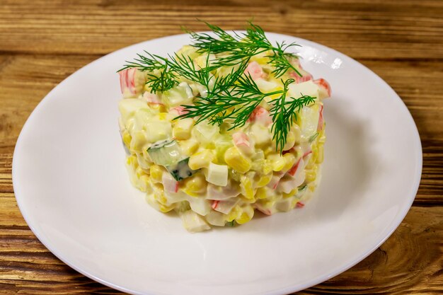 Salad with crab sticks sweet corn cucumber eggs and mayonnaise on wooden table