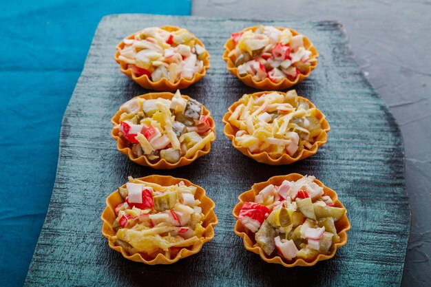 Salad with crab in tartlets on a black board.