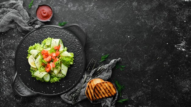 Salad with cucumber salmon and lettuce Healthy food On a black stone plate Top view