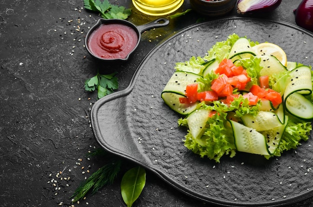 Salad with cucumber salmon and lettuce Healthy food On a black stone plate Top view