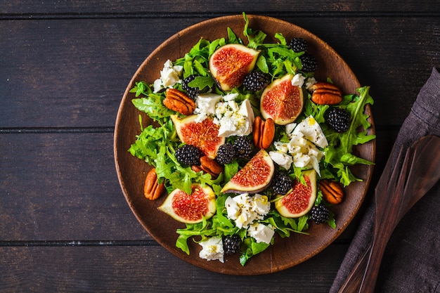 Salad with figs, feta cheese and blackberries in a wooden plate on dark