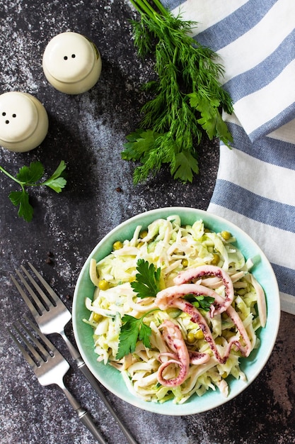 Salad with fresh cabbage cucumber green peas and octopus in a bowl on a dark countertop Top view flat lay