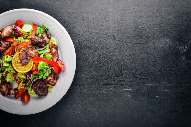 Salad with fresh cucumbers tomatoes and greens with grilled meat on a plate Wooden board Top view Free space