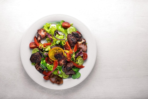 Salad with fresh cucumbers tomatoes and greens with grilled meat on a plate Wooden board Top view Free space