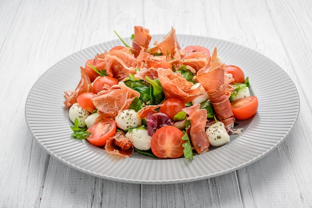 Salad with fresh vegetables with dried tomatoes, meat and mustard, mozzarella, prosciutto