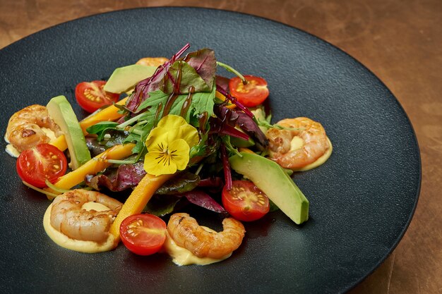 Insalata con gamberi fritti, rucola, pomodorini, avocado e mango in un piatto di ceramica nera