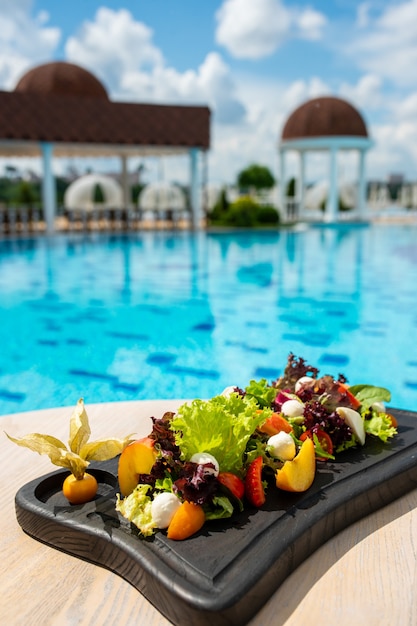 Salad with fruits vegetables cheese on a black wooden board Luxury resort with pool view