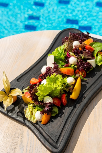 Salad with fruits vegetables cheese on a black wooden board Luxury resort with pool view