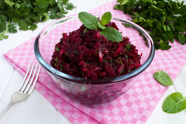 Foto insalata con barbabietole ed erbe grattugiate nella ciotola di vetro sullo sfondo di legno bianco