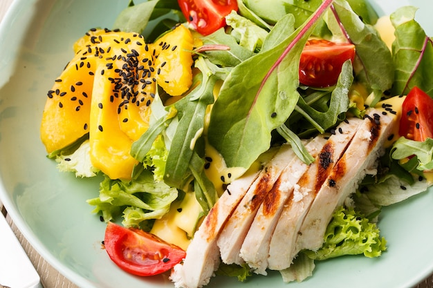 Salad with grilled chicken, mango, lettuce, avocado, tomatoes, arugula, cheese sause on a white plate