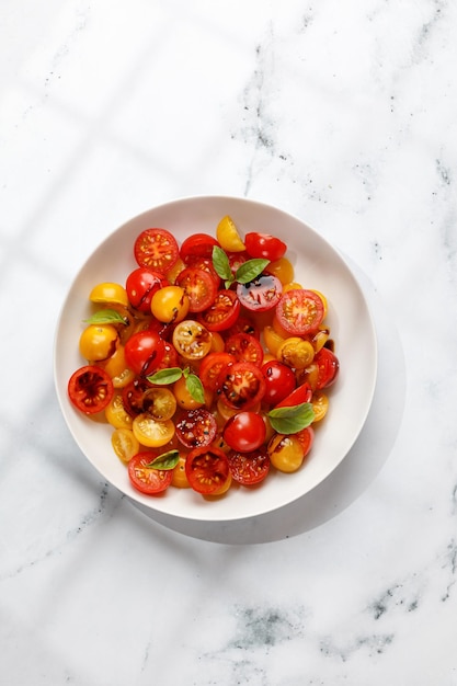 Salad with halves of red and yellow tomatoes cherry with basil topping balsamic sauce on white plate