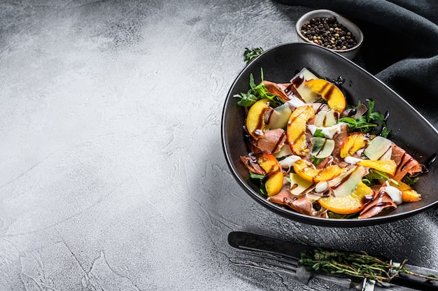 Salad with ham, peach and arugula. Cold snacks. Gray background. Top view. Copy space