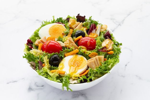 Салат с салатом, яйцом, тунцом, оливками и медово-горчичным винегретом на белом фоне