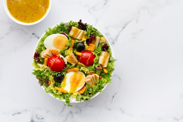 Salad with lettuce egg tuna olives and honey and mustard\
vinaigrette on white background