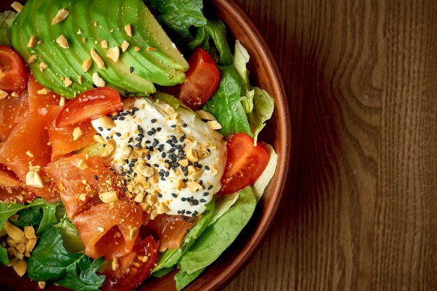 Salad with lightly salted salmon and poached egg in a plate on a wooden background