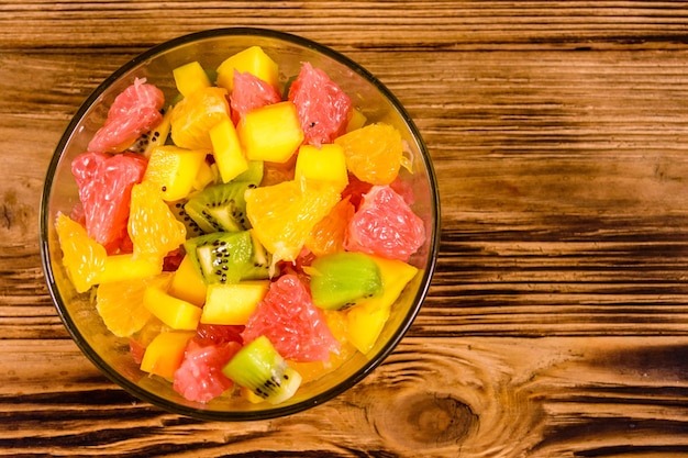 Salad with mango, oranges, grapefruit and kiwi fruits in a glass bowl on wooden table. Top view