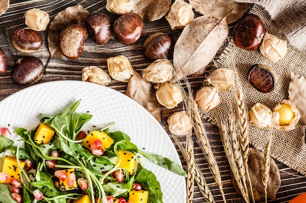 Insalata con mango, zucca arrostita, rucola, semi di melograno sdraiato sul piatto bianco.