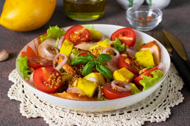 Insalata con pollo affumicato al mango e pomodorini servita con foglie di lattuga verde in un piatto su fondo marrone