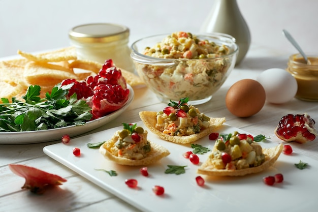 Insalata con maionese, piselli e verdure lesse su fette biscottate, decorata con semi di melograno e prezzemolo